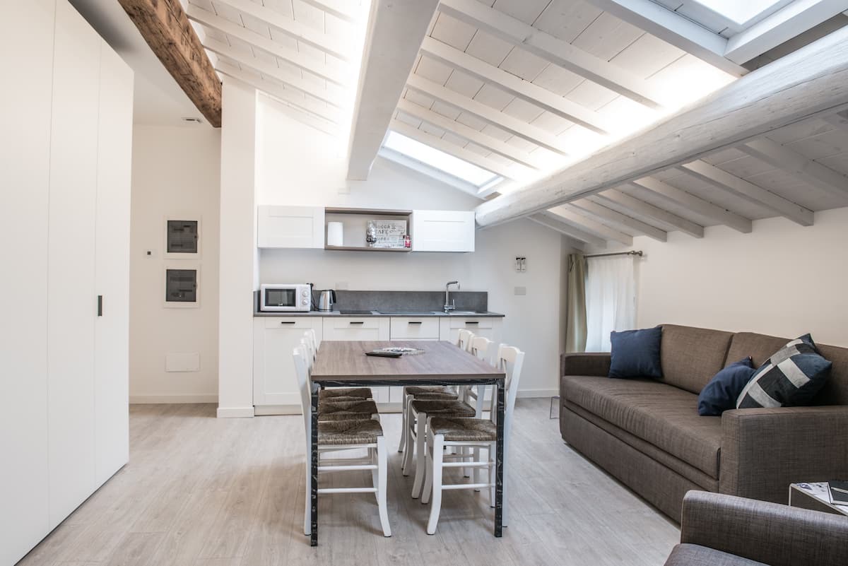 Luminoso espacio abuhardillado de planta abierta con cocina blanca, mesa de comedor y sofá gris