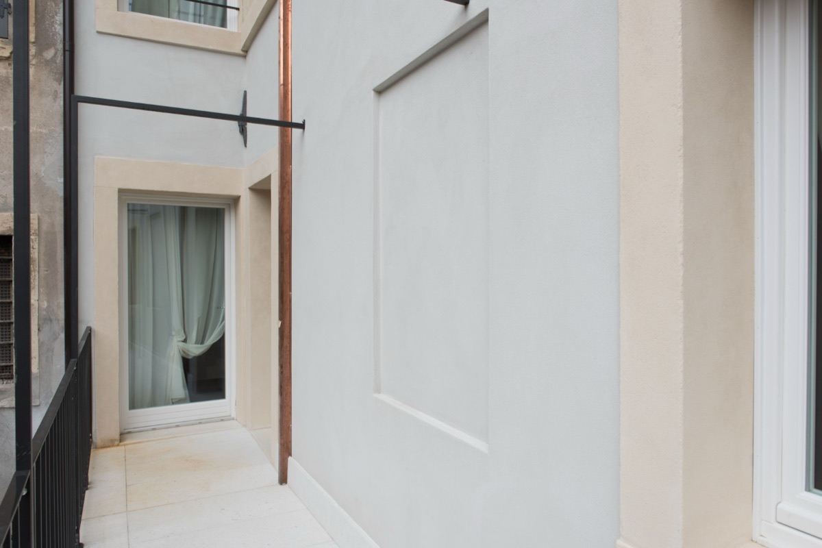Pasarela exterior con suelo de piedra clara y la puerta acristalada del apartamento